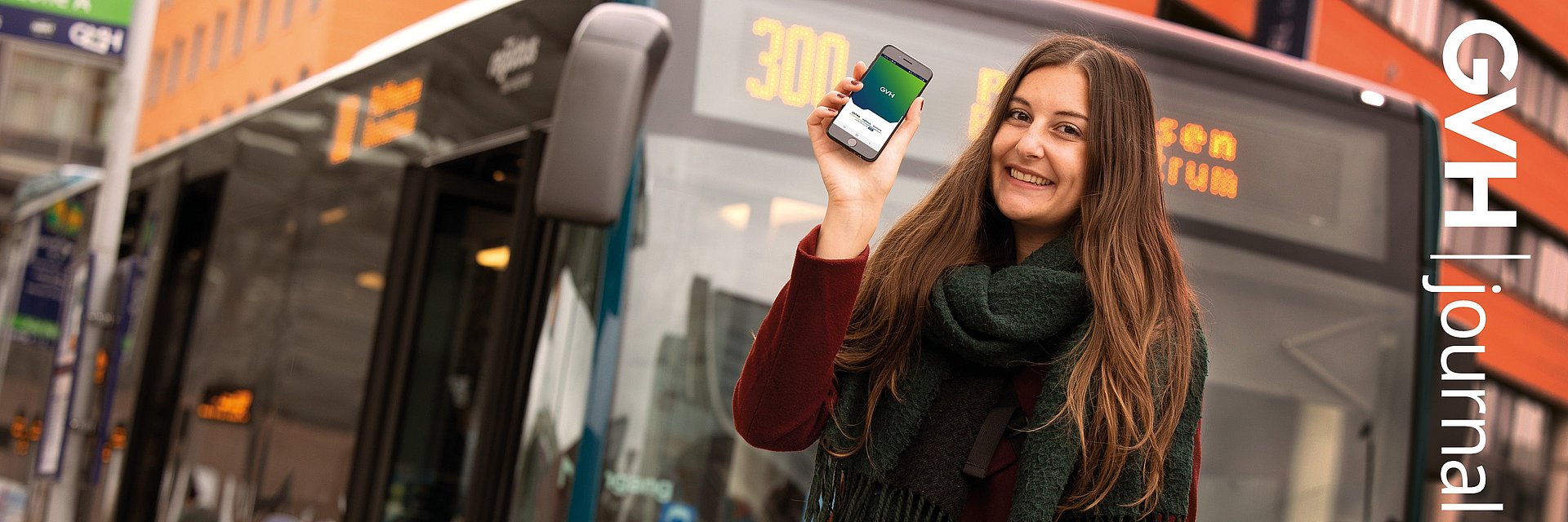 Titel des GVHjournals 4.2021: Eine Frau steht einem Handy in der Hand vor einem Bus