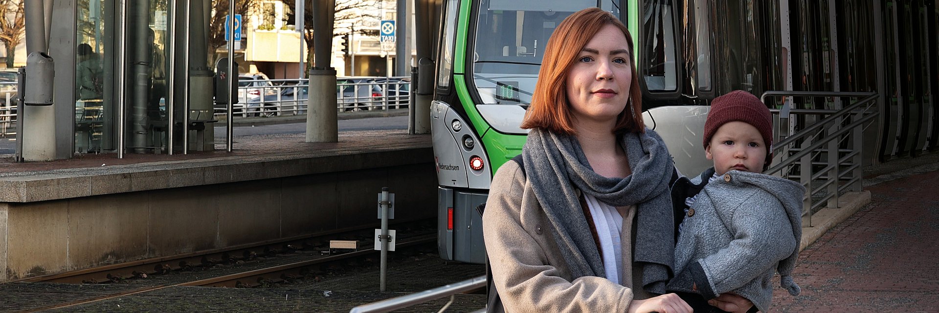 Titel des GVH journal 01.2022: Eine Frau hält ihr Kind auf dem Arm und schaut in die Kamera. Im Hintergrund fährt eine Stadtbahn ein.