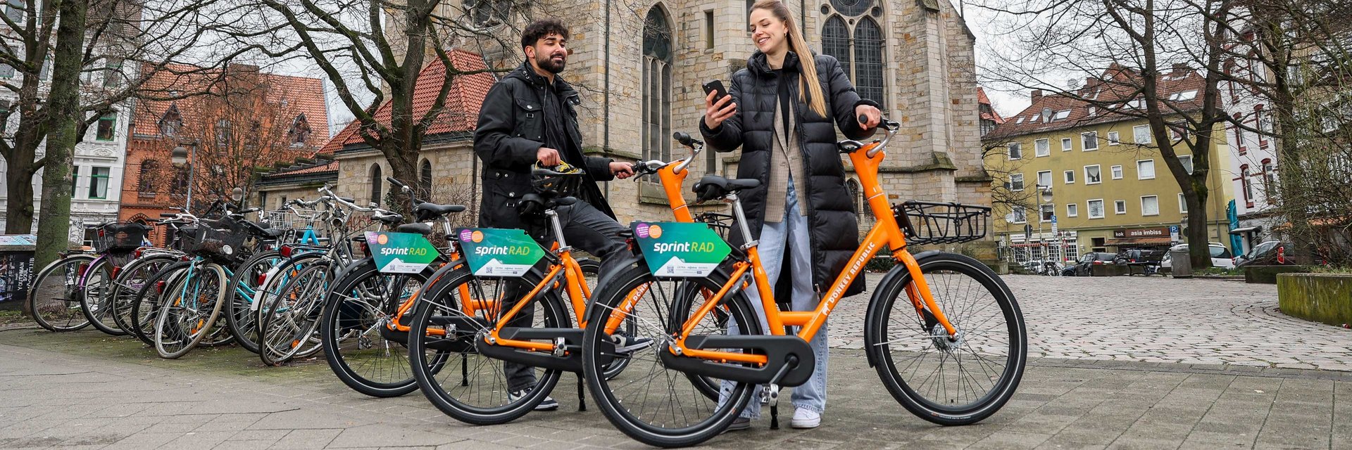Ein Mann und eine Frau stehen an zwei Fahrrädern. Im Hintergrund befindet sich die Lutherkirche in Hannover.