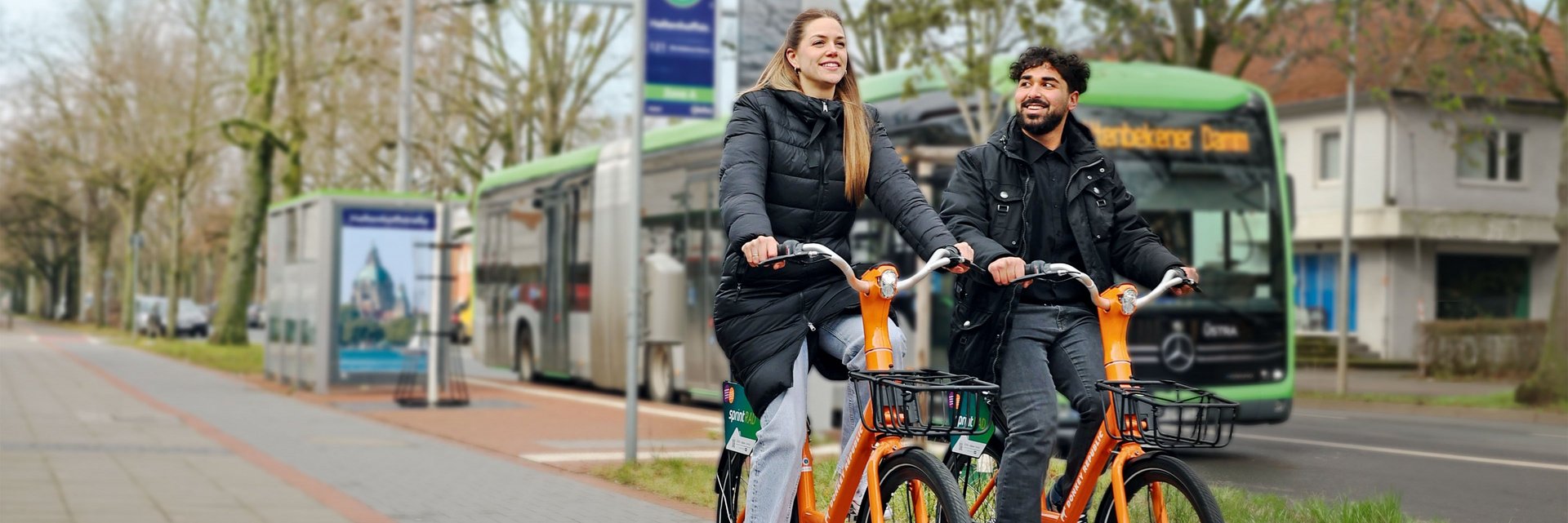 Coverbild des GVH journals 01.2024: Zwei Personen fahren jeweils auf einem orangenen Fahrrad an einer Bushaltestelle vorbei.