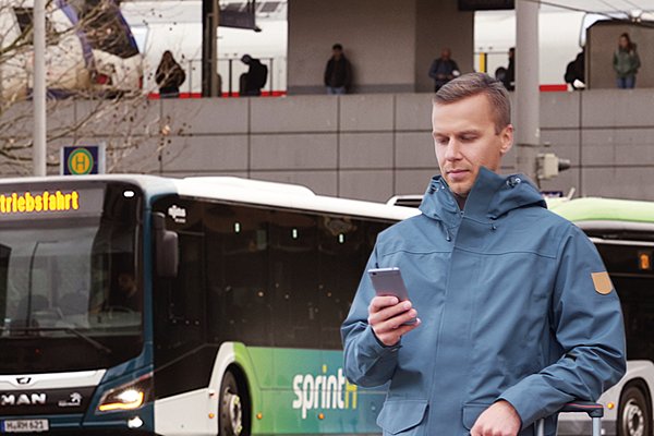 Coverbild des GVH journals 01.2021: Ein Mann steht mit einem roten Rollkoffer an einer Haltestelle und schaut auf sein Handy. Im Hintergrund sieht man mehrere Busse und den Hauptbahnhof.