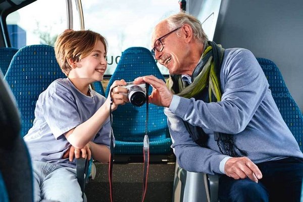 Coverbild des GVH journals 02.2023: Ein Großvater und sein Enkel sitzen in einem Bus und schauen sich gemeinsam Fotos auf einem Kameradisplay an.