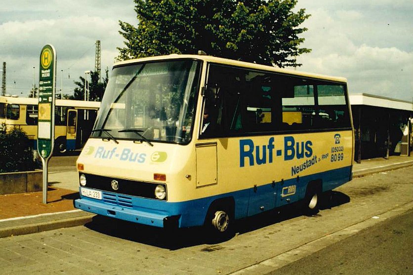 Bild von einem alten Rufbus Neustadt, der vor einer Haltestelle steht. Im Hintergrund ist ein weiterer Bus zu sehen. 